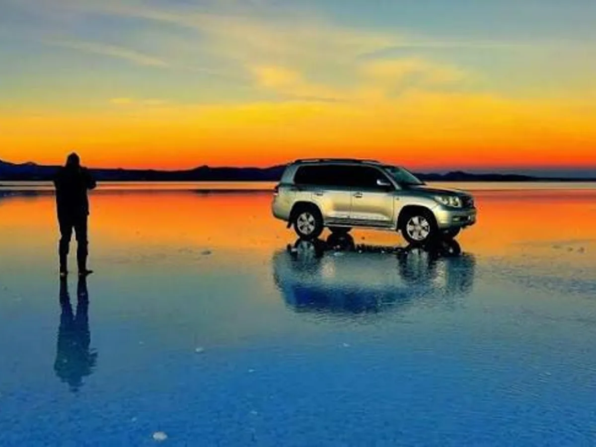 A 4x4 and its reflection on the flooded salt flats at sunset